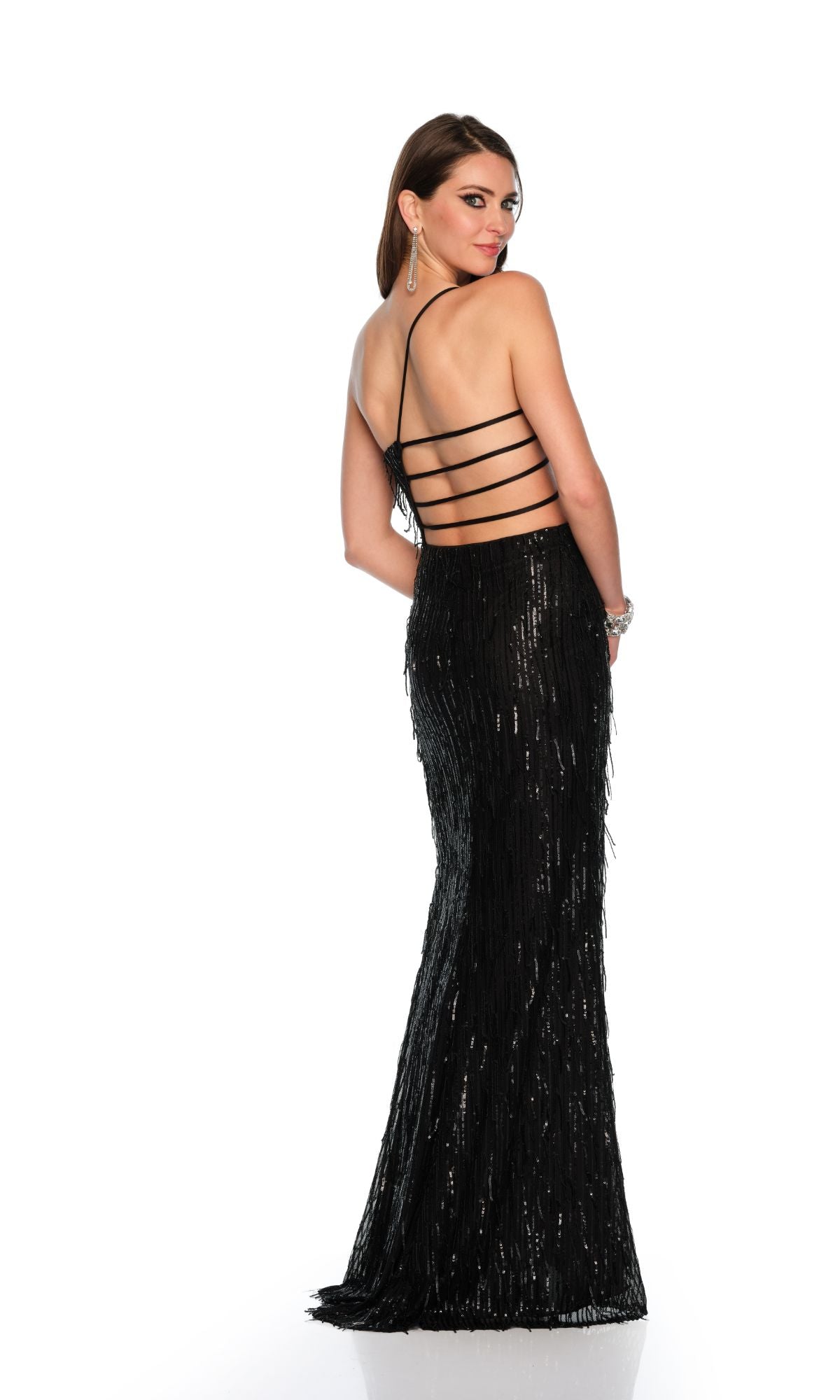 A woman in the Long Formal Dress 11302 by Dave and Johnny—a black, floor-length sequined gown with a fitted silhouette and strappy open back—stands facing away, glancing over her shoulder against a white background.